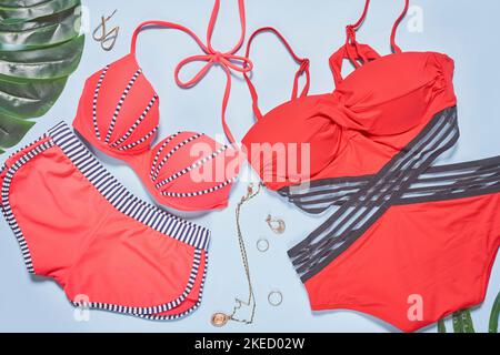 due costumi da bagno, uno in rosso e l'altro in nero su sfondo bianco con foglie di palma accanto ad esso Foto Stock