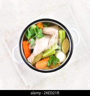 Brodo di pollo con verdure e spezie in pentola su fondo di pietra chiara. Vista dall'alto, disposizione piatta Foto Stock