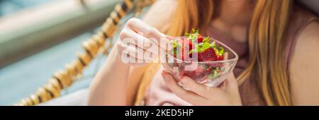 Ritratto di splendida donna che indossa bel vestito seduto in un patio e mangiare STRISCIONE fragola, FORMATO LUNGO Foto Stock