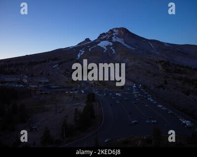 Parcheggio ai piedi di una grande montagna coperta di neve. Molte auto. Piccoli pini. Crepuscolo. Bellissima natura, posto di villeggiatura. Ecologia, infrast Foto Stock