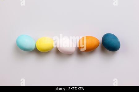 Una vista dall'alto di uova di Pasqua dipinte di colore disposte in una linea con uno sfondo bianco Foto Stock