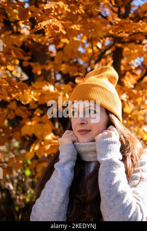 Una donna in un berretto arancione davanti alle foglie di arancio guardando via Foto Stock