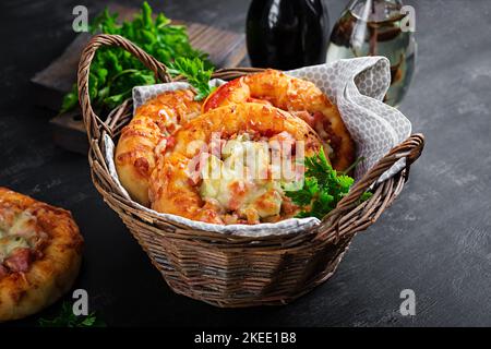 Mini pizza per bambini, piccole torte aperte con prosciutto, salsa di pomodoro, mozzarella e formaggio in cestino su fondo scuro. Foto Stock