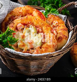 Mini pizza per bambini, piccole torte aperte con prosciutto, salsa di pomodoro, mozzarella e formaggio in cestino su fondo scuro. Foto Stock