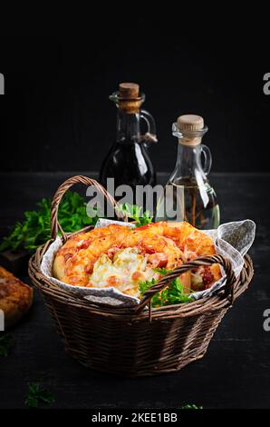 Mini pizza per bambini, piccole torte aperte con prosciutto, salsa di pomodoro, mozzarella e formaggio in cestino su fondo scuro. Foto Stock