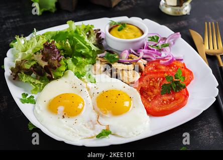 Cibo chetogenico. Uova fritte, funghi e pomodori a fette. Keto, colazione al paleo. Foto Stock