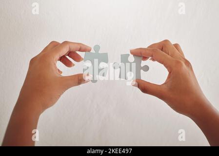 Mettere insieme i pezzi. Un giovane designer non identificabile che tiene due pezzi di puzzle contro una parete bianca in ufficio. Foto Stock