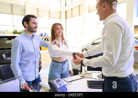 Venditore che si congratula con la cliente femmina per l'acquisto di una nuova vettura Foto Stock