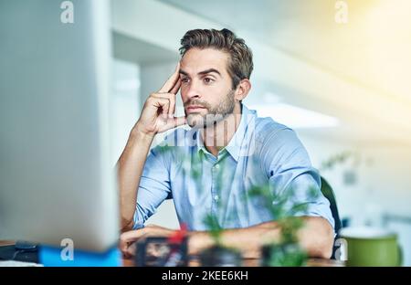 Perso in pensieri di successo. Un giovane uomo d'affari che lavora su un computer in un ufficio. Foto Stock