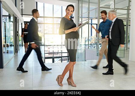 Per un look di grande impatto in ufficio. Ritratto di una donna d'affari incinta in piedi in un ufficio occupato. Foto Stock
