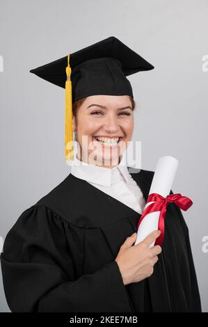 Donna sorridente con diploma di laurea in possesso di abito su sfondo bianco. Foto verticale. Foto Stock