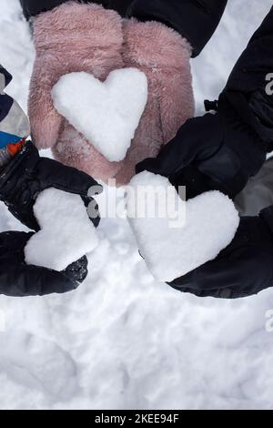 Amore Inverno. Le mani di due adulti e di un bambino in mitrine tengono 3 cuori di neve. Vacanze nella stagione invernale, stile di vita attivo. Famiglia cordiale. Neve Foto Stock