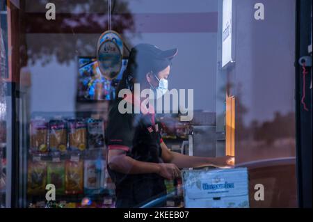 Un'impiegato femminile del minimarket, che indossa una maschera facciale, lavora sul lungofiume durante la pandemia COVID - 19. Phnom Penh, Cambogia. © Kraig Lieb Foto Stock