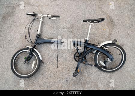 Vecchia bicicletta con un telaio rotto a metà steso su un asfalto Foto Stock