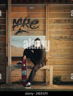 Un pattinatore seduto su una panca di fronte alla parete di legno in graffiti. Foto Stock