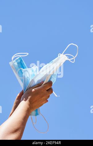 la mano di qualcuno che tiene una maschera blu e bianca a forma di aquilone contro un cielo blu chiaro Foto Stock