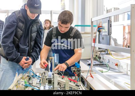 12 novembre 2022, Brandeburgo, Schwarze Pumpe: Nell'armadio dell'elettronica, Vincent Adamsky (r), un tecnico dell'elettronica per la tecnologia operativa del secondo anno di formazione, mostra Mika Räum, interessata alla formazione a LEAG, un modello di un sistema di smistamento. In questo caso, diverse barriere fotoelettriche vengono utilizzate per rilevare e ordinare gli oggetti in base alla loro riflessione. La Lausitz Energie Bergbau AG e la Lausitz Energie Kraftwerke AG (LEAG) stanno organizzando una giornata all'aperto nel parco industriale Schwarze Pumpe, dove gli interessati possono guardare le spalle di tirocinanti e istruttori. LEAG sta cercando di riempire 100 v Foto Stock