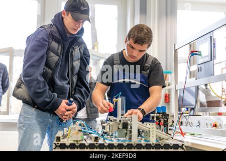 12 novembre 2022, Brandeburgo, Schwarze Pumpe: Nell'armadio dell'elettronica, Vincent Adamsky (r), un tecnico dell'elettronica per la tecnologia operativa del secondo anno di formazione, mostra Mika Räum, interessata alla formazione a LEAG, un modello di un sistema di smistamento. In questo caso, diverse barriere fotoelettriche vengono utilizzate per rilevare e ordinare gli oggetti in base alla loro riflessione. La Lausitz Energie Bergbau AG e la Lausitz Energie Kraftwerke AG (LEAG) stanno organizzando una giornata all'aperto nel parco industriale Schwarze Pumpe, dove gli interessati possono guardare le spalle di tirocinanti e istruttori. LEAG sta cercando di riempire 100 v Foto Stock