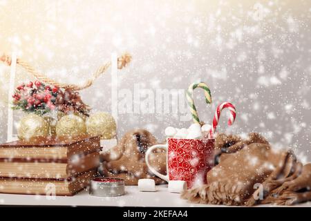 Buon Natale. Tazza con marshmallow e pila di libri con nevicate sfocate. Foto Stock