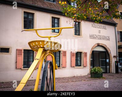 Rouffach, Francia - 11 ottobre 2022: Una grande bicicletta gialla storica di fronte a un centro culturale e centro di servizi a Rouffach, Alsazia Foto Stock