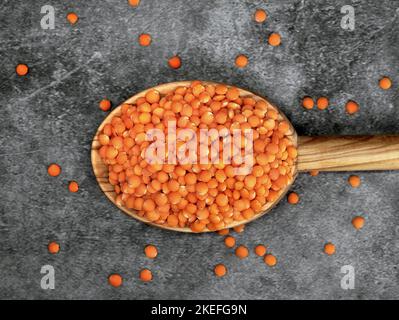 Lenticchie rosse in un cucchiaio da cucina in legno su sfondo grigio, sano concetto di cibo vegano con alte proteine Foto Stock