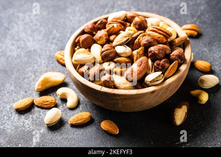 Assortimento di dadi in ciotola di legno su tavola di pietra scura. Anacardi, nocciole, mandorle, noci brasiliane e noci pecan. Foto Stock