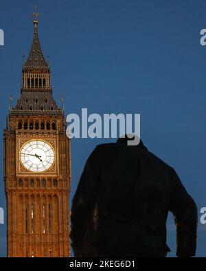 Londra, Regno Unito. 12th Nov 2022. L'iconica Torre Elisabetta, la torre dell'orologio conosciuta anche come Big ben presso il Parlamento, si erge illuminata contro il cielo blu chiaro con la statua di Winston Churchill sulla Piazza del Parlamento proprio di fronte. Un giorno di novembre insolitamente caldo e soleggiato si chiude a Westminster, Londra. Credit: Imageplotter/Alamy Live News Foto Stock