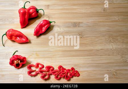 Capsicum chinense 'Scotch Bonnet' intero e affettato su un tavolo di legno Foto Stock