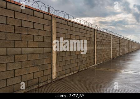 Muro di mattoni che si perde dalla vista lungo, dotato nella sua parte superiore di concertina, fili con lame di taglio. Foto Stock
