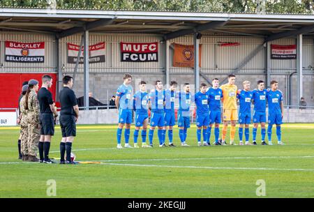 Broadhurst Park, Manchester, Lancashire, Regno Unito. 12th Nov 2022. Regno Unito, Warrington - Rylands squadra di calcio si trovano intorno al cerchio centrale del campo al FC United di Manchester come una giovane donna Army Cadet e i funzionari si uniscono alla squadra per l'ultimo posto e un minuto di silenzio in memoria dei caduti nelle guerre. Credit: John Hopkins/Alamy Live News Foto Stock