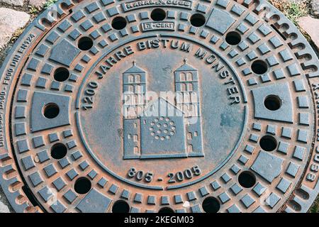 25 luglio 2022, Munster, Germania: Coperchio o portello della fogna con l'emblema o lo stemma di Muenster a strada della città Foto Stock