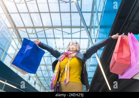 Donna anziana felice con borse di shopping sorridente durante le feste salse di festa. Donna che celebra eccitato. Foto Stock