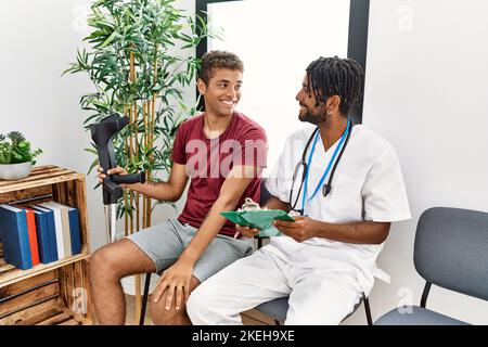 Due uomini fisioterapista e paziente che hanno consultazione medica utilizzando stampelle in sala d'attesa ospedale Foto Stock