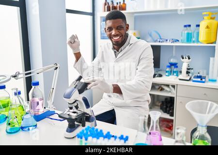 L'uomo afroamericano che lavora al laboratorio di scienziato urlando orgoglioso, celebrando la vittoria e il successo molto eccitato con il braccio sollevato Foto Stock