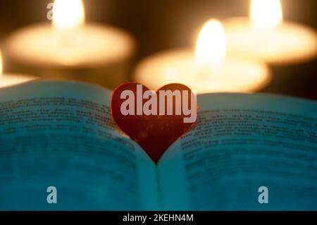 Forma a cuore rosso sulla Sacra Bibbia con sfondo a luci di candela. Spazio personalizzabile per testo o idee. Spazio di copia. Foto Stock