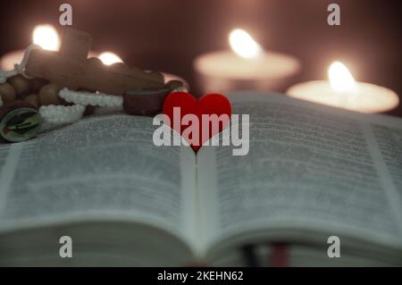 Forma a cuore rosso sulla Sacra Bibbia con luci a candela e sfondo di colore vintage. Spazio personalizzabile per testo o idee. Spazio di copia. Foto Stock