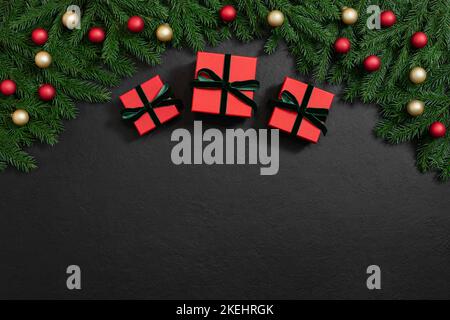Bordo natalizio con regali, rami di abete, baubles rosso e oro su sfondo nero. Spazio per il testo. Concetto invernale. Biglietto d'auguri. Spazio copia, temp Foto Stock