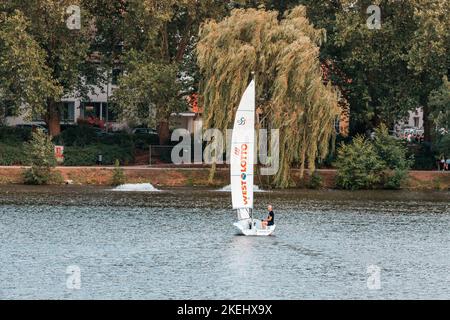 25 luglio 2022, Munster, Germania: Uomo impegnato in nautica da diporto vela sportiva su un lago Aasee in città park25 luglio 2022, Munster, Germania: Molte barche a vela e o Foto Stock