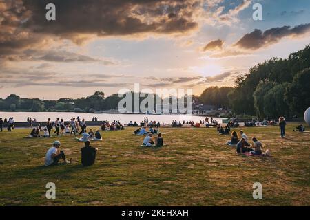 25 luglio 2022, Munster, Germania: Persone che riposano nel parco cittadino di Munster e guardano il tramonto sul lago Aasee Foto Stock