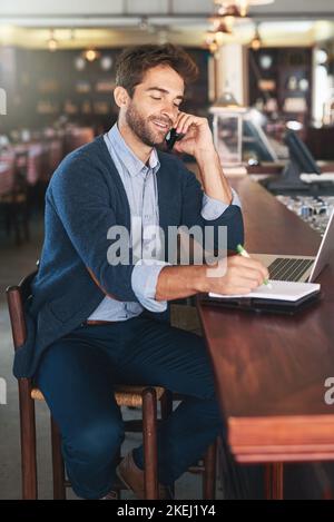 Certo... che è il numero. Un bel giovane che usa il suo portatile e il cellulare in un bar. Foto Stock