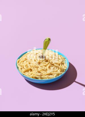 Ciotola con spaghetti Cacio e Pepe in luce brillante su un tavolo di colore viola. Delizioso e semplice piatto di pasta italiana, spaghetti con parmigiano e nero Foto Stock