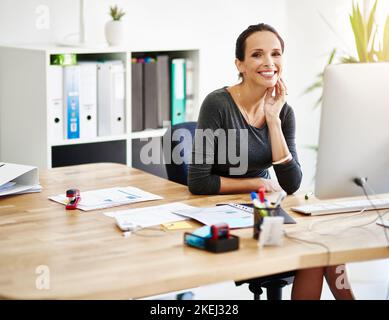 Messaggi istantanei in cima a tutte le mie scadenze. Ritratto corto di una donna d'affari attraente seduta alla sua scrivania in ufficio. Foto Stock