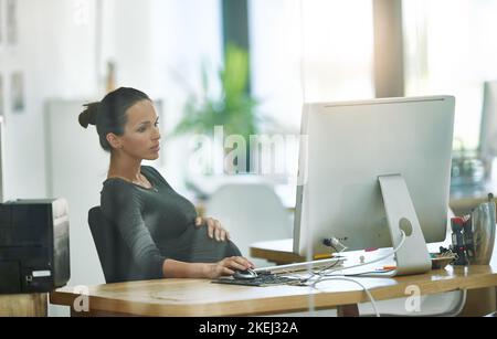 Assicurisi che tutto è in ordine durante il suo congedo di maternità. Una donna d'affari incinta che lavora al suo calcolatore nell'ufficio. Foto Stock