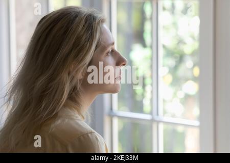 Triste giovane donna che guarda fuori finestra sembra allegro e melanconico Foto Stock