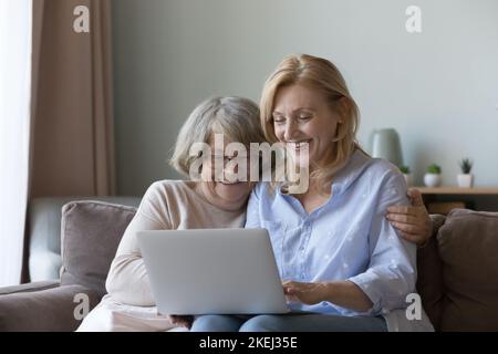 La figlia matura e la madre anziana siedono sul divano con il laptop Foto Stock