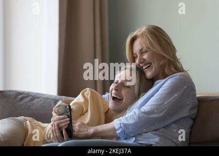 Donna ridente sua figlia che riposa in casa guardare video utilizzare smartphone Foto Stock