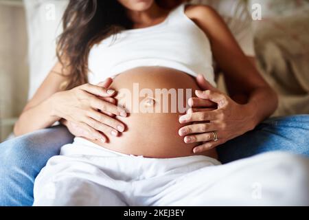 Legarsi con il loro fascio di gioia. Primo piano di un marito e di una moglie che tengono insieme il ventre incinta. Foto Stock