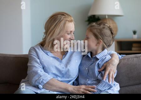 La nonna di mezza età abbraccia la sua nipote siedasi insieme sul divano Foto Stock