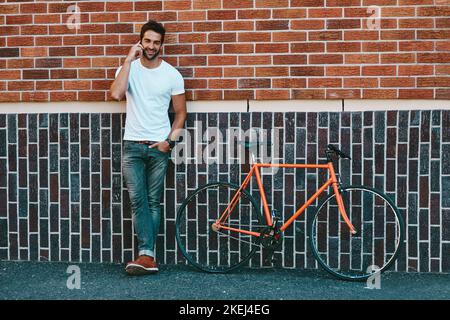 Il ragazzo più cool e connesso della città, un bel giovane in piedi accanto alla sua bicicletta e con un telefono in città. Foto Stock