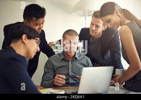 Si sentono sempre motivati a dare il meglio di sé. Un gruppo di colleghi che discutono di qualcosa su un notebook durante una riunione. Foto Stock